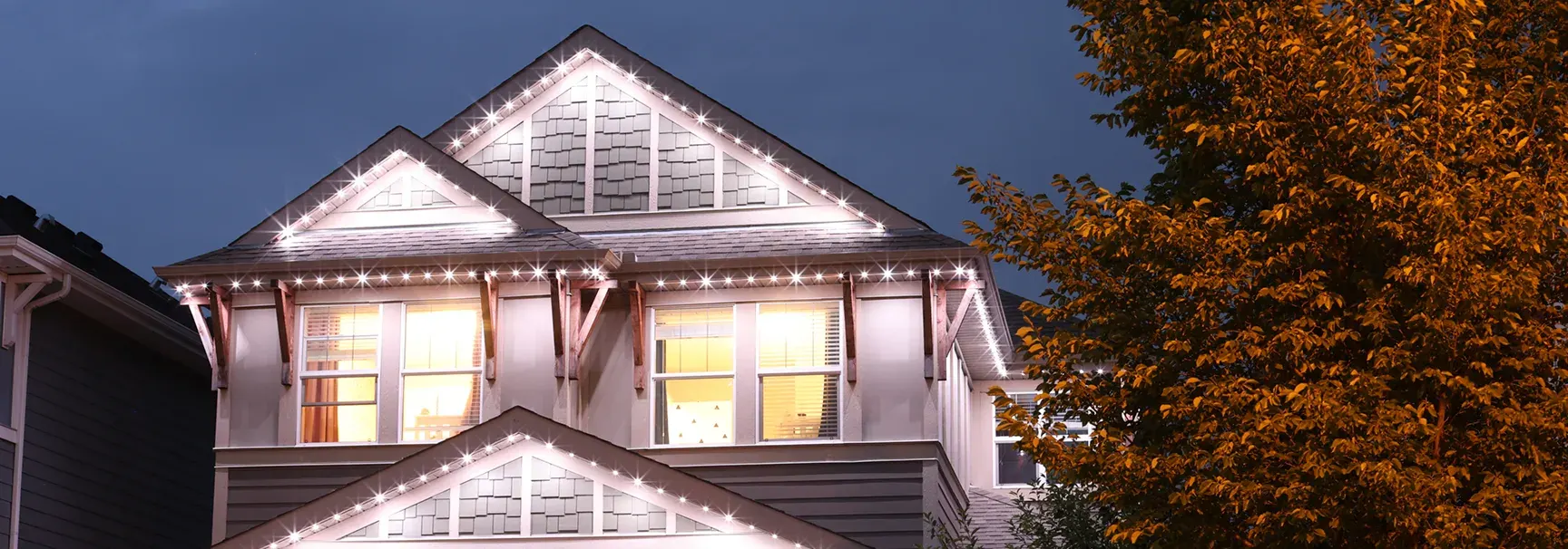 A two-storey Western Canada home at night with permanent white LED lights tracing every roofline and gable